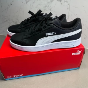 Svarta Puma sneakers med vit sula - Stilrena svarta sneakers från Puma med vit sula och vit sidostripes. Skorna har klassisk låg profil, snörning och mjuk innersula med SoftFoam+ för extra komfort. Perfekta för dig som gillar enkel och sportig stil.