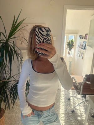Vit ribbad långärmad topp - Säljer en vit ribbad långärmad topp med rundad, djup urringning och mörkblå spetskant runt halsen. Toppen är figurnära och har långa ärmar. Perfekt att styla med jeans för en enkel och snygg look. Storlek xxs, HM