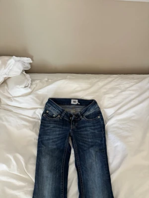 Mörkblå bootcut jeans - Säljer ett par mörkblå bootcut jeans med klassisk femficksmodell och snygga slitningar framtill. Jeansen har låg midja och kontrastsömmar. Perfekta för dig som gillar en avslappnad men ändå trendig look.