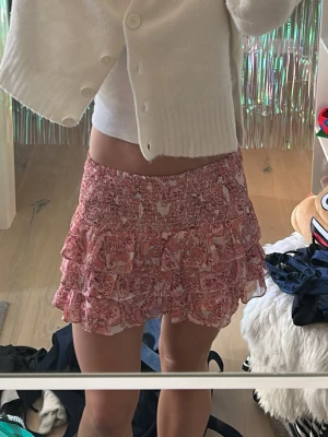Rosa kjol - Supersöt kort kjol i rosa med blommigt mönster och flera volanger. Använd väldigt få gånger