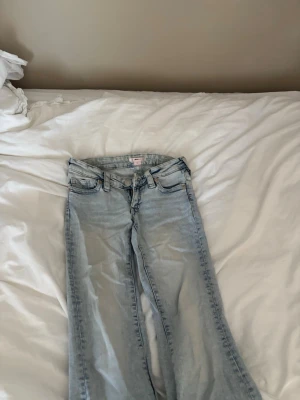Ljusblå bootcut jeans - Säljer ett par ljusblå bootcut jeans med klassisk femficksdesign och snygga detaljer på bakfickorna. Jeansen är lågmidjade midja och är tillverkade i ett mjukt denimtyg som ger en avslappnad vibe. Perfekta till sneakers eller boots för en cool look💞