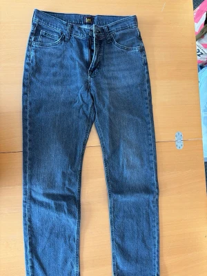 Mörkblå raka jeans från Lee - Klassiska svarta stentvättade jeans från Lee med rak passform och fem fickor. Jeansen har en tidlös look med subtila slitningar och är tillverkade i ett slitstarkt denimtyg. Perfekta för dig som gillar enkel och clean stil.