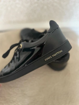 Louis Vuitton Frontrow  - Populära Frontrow sneakers från Louis Vuitton i glansigt material med svarta skosnören och guldfärgade detaljer. Diskret Louis Vuitton-logga på sidan av sulan. Perfekta för dig som gillar exklusiv och stilren design. Äkta. Köpta i Louis Vuitton butiken i Berlin. Frontrow kostar i butik på ca 800euro! Ingen box.
