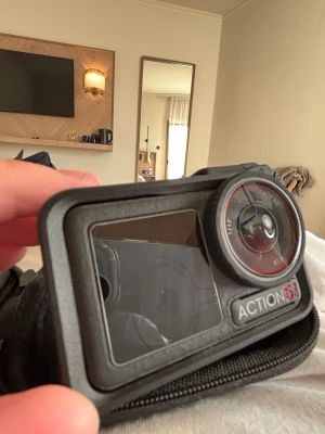DJI Osmo 5 pro - Action 5S är en kompakt digitalkamera med robust svart hölje och stor lins framtill. Kameran har en tydlig display på baksidan och är designad för att tåla tuffa tag, perfekt för äventyr och actionfyllda aktiviteter.