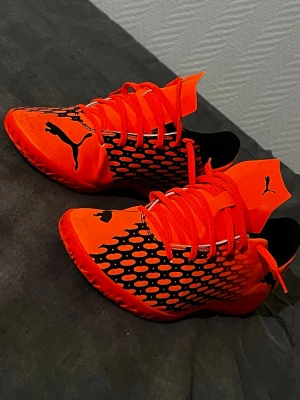 Orangea fotbollsskor från Puma - Säljer ett par riktigt snygga  från Puma i en skarp orange färg med svarta detaljer och mönster. Skorna har låg profil, snörning och är tillverkade i syntetmaterial förutom bra grepp och känsla på planen. Perfekta för dig som vill sticka ut på matchen.