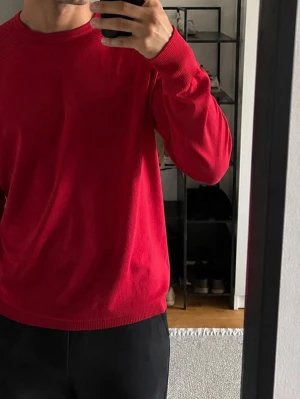 Röd stickad tröja från H&M - Snygg röd stickad tröja från H&M med rund halsringning och ribbade muddar vid ärmslut och nederkant. Tröjan har en enkel och stilren design, perfekt för att addera färg till din outfit. Materialet ser mjukt och bekvämt ut, och modellen är långärmad.