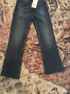 Mörkblå raka jeans från Zara - Säljer ett par mörkblå jeans från Zara med rak passform och råa, avklippta benslut. Jeansen har klassisk femficksdesign och subtila slitningar framtill för en trendig look. Perfekta till en avslappnad stil.