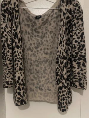 Leopardmönstrad stickad tröja H&M - Snygg stickad tröja från H&M med leopardmönster i svart och beige. Tröjan har rund halsringning och trekvartsärmar. Perfekt för dig som vill ha en trendig och bekväm look. Materialet känns mjukt och lätt.