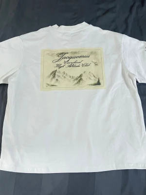Vit Jacquemus t-shirt med tryck - Säljer en vit t-shirt från Jacquemus med tryck på ryggen och liten logga framtill. T-shirten har korta ärmar och är gjord i mjuk bomull. Perfekt för dig som gillar stilrena plagg med exklusiv känsla.