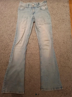 Ljusblå bootcut jeans - Säljer ett par ljusblå bootcut jeans med klassisk femficksmodell och knappgylf. Jeansen har en lätt tvättad look och är tillverkade i denim med lite stretch för skön passform. Perfekta till sneakers eller boots. Från H&M, storlek 170