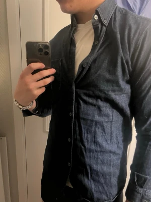 Mörkblå skjorta  - Säljer en mörkblå skjorta i mjuk bomull med klassisk knappslå och bröstficka. Skjortan har lång ärm och button-down krage, perfekt för en avslappnad men ändå stilren look. Skriv om du har frågor