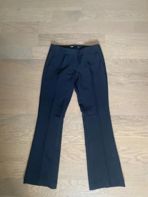 Low waist kostymbyxor från Bikbok - Snygga svarta kostymbyxor med utsvängda ben och pressveck. Byxorna har fickor fram och passpoalfickor bak samt hällor för skärp. Perfekta för en stilren och trendig look.