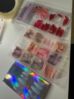 Mixade press-on naglar i olika färger - Säljer flera set press-on naglar i olika färger och former. Innehåller bland annat röda, rosa, nude, lila och blå naglar, vissa med dekorationer. Naglarna är både spetsiga och mandelformade. Perfekt för dig som vill variera din nagellook snabbt och enkelt.