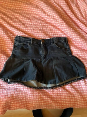 Mörkblå mini jeanskjol med volang - Säljer en mörkblå kort jeanskjol med volangkant och klassiska fickor både fram och bak. Kjolen har bälteshällor och knappstängning framtill. Perfekt för dig som gillar en trendig och avslappnad stil.
