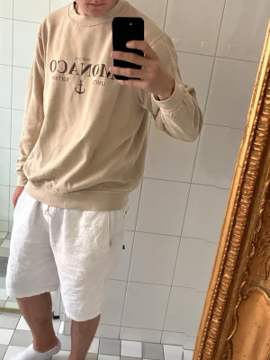 Beige stickad tröja boohooMAN - Beige stickad tröja från boohooMAN med tryck framtill där det står 'MONACO LIMITED EDITION' och ett litet ankare. Tröjan har rund hals, ribbade muddar och avslappnad passform. Perfekt för dig som gillar enkel och clean stil.