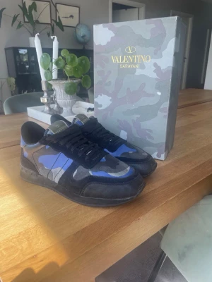 Valentino Rockrunners  - Snygga sneakers från Valentino Garavani i svart och mörkblå camo-design. Skorna har lågt skaft, klassisk snörning och detaljer i mocka och läder. Kommer med originalkartong och röd dustbag med logga. Pris kan diskuteras!