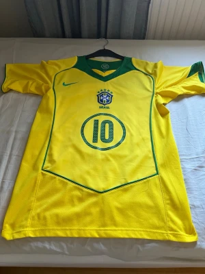 Brasilien fotbollströja Ronaldinho #10 - Gul Brasilien fotbollströja köpt från fotbollsmarknaden ny pris 549 kr storlek s har man xs så kommer den sitta perfekt också. Använd cirka 2 gngr säljer då den inte passar längre. Fasta priset är 400 men är villig att gå ner vid snabb affär 