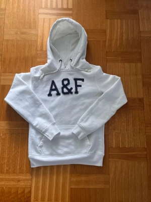 Abercrombie and Fitch - Säljer en Abercrombie and Fitch- hoodie med stor A&F-brodyr i mörkblått på bröstet. Hoodien har huva med dragsko och en klassisk magficka. Mjuk och skön, perfekt för chill dagar. Materialet känns fleeceaktigt och ger en mysig känsla.