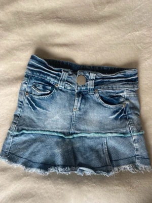 Blå jeanskjol med rå kant - Storlek 9/10 så ungefär xxxs, finns en liten fläck på insidan av kjolen!