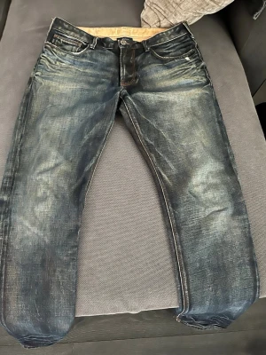 Vintage Armani Jeans - Säljer ett par snygga mörkblå jeans från Armani med slitna detaljer och klassisk femficksmodell. Jeansen har en normal passform. Perfekta för dig som gillar en avslappnad men stilren look. Hör av dig vid funderingar