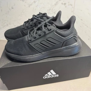 Svarta Adidas sneakers - Helt Ny Snygga helsvarta sneakers från Adidas med mesh-ovandel och robust sula. Klassisk design med tre ränder på sidan och snörning. Perfekta för dig som gillar stilrena och sportiga skor.