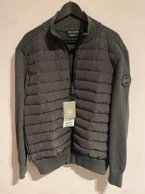 Grå cardiganjacka från Canada Goose - Grå cardiganjacka från Canada Goose med quiltad front och stickade ärmar.                             🚨Passar till de som bär på storlek L (mindre en än standard storlek XL) 🚨pris kan diskuteras vid snabbt köp 🙌 