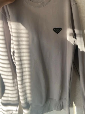 Beige sweatshirt med patch - Stilren beige sweatshirt med rund hals och ribbade muddar. Tröjan har en svart patch med logga på bröstet och är tillverkad i mjukt material. Perfekt för en avslappnad och trendig look.
