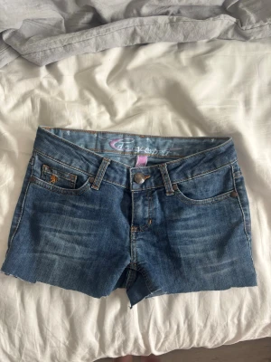 Blå jeansshorts från edc by esprit - Snygga blå jeansshorts från edc by esprit med klassisk femficksdesign och rå kant nedtill. Shortsen har orangea kontrastsömmar och knappgylf. Perfekta för varma dagar och ger en avslappnad look. Storlek 26/30 (xxs?) säljer då de tyvärr är för små