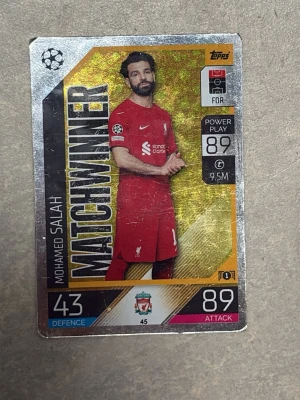 Match Attax Mohamed Salah kort - Säljer ett Match Attax samlarkort med Mohamed Salah från Liverpool FC. Kortet har guldfärgad bakgrund, texten MATCHWINNER och visar Salah i röd matchtröja. Kortet har stats som 89 attack och 43 defence. Perfekt för dig som samlar på fotbollskort!