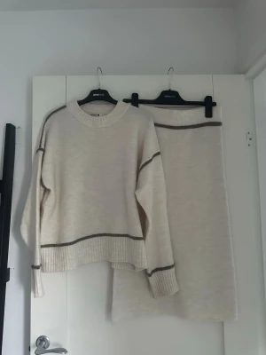 Beige stickat sett med bruna ränder - Beige stickad kjol med en rak passform och mörkbruna ränder upptill. Kjolen är mjuk och har en enkel, stilren look som passar perfekt till höst och vinter. Matcha gärna med en stickad tröja för en mysig outfit. Skulle också funkat för dig som har storlek Xs. Aldrig använt 
