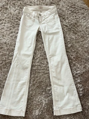Vita bootcut jeans från Nelly - Säljer ett par vita bootcut jeans med klassiska fem fickor och dragkedja fram. Jeansen är låg i midjan och har utsvängda ben och detaljerade sömmar. Storleken är i ”32 short”.