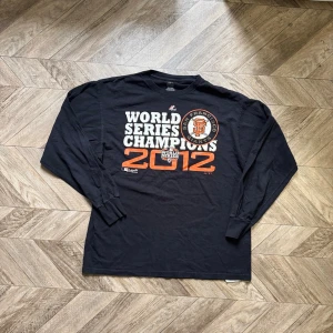 Svart långärmad Giants t-shirt - Säljer en svart långärmad t-shirt från Majestic med San Francisco Giants World Series Champions 2012-tryck framtill. Skön passform och perfekt för dig som gillar baseball eller vill ha en sportig stil.