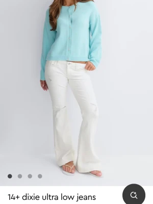 Vita bootcut jeans - Säljer ett par vita jeans med ultra låg midja och bootcut passform. Jeansen har diskreta slitningar och coola sömmar på bakfickorna. Perfekta för dig som gillar en trendig och avslappad stil. 