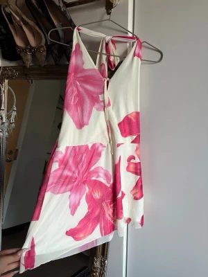 Somrig Halterneck klänning - Jättefin halterneck klänning med liljor på. Den är lite off white- pastell gul. Helt oanvänd