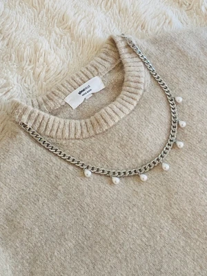 Silverfärgat halsband med pärlor - Snyggt halsband i silverfärgad rostfritt med kedjedesign och små vita pärlor som hänger längs hela kedjan. Perfekt för att ge din outfit en trendig touch. Passar till många olika stilar och är lätt att matcha med andra accessoarer.
