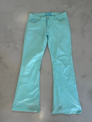 Turkosa bootcut jeans med patchdetaljer - Snygga turkosa jeans med bootcut-modell och unika patchdetaljer på bakfickorna. Jeansen har klassisk femficksdesign, bälteshällor och knappgylf. Materialet ser ut att vara bomull med lite stretch för extra komfort.