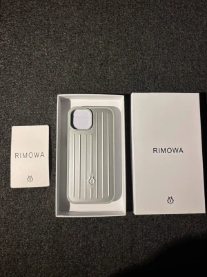 RIMOWA mobilskal iPhone 15 - Snyggt silverfärgat mobilskal från RIMOWA i aluminium med klassisk räfflad design och logga längst ner. Skalets form är anpassad för moderna smartphones och ger en exklusiv känsla. Perfekt för dig som vill ha ett stilrent och tåligt skydd till mobilen.