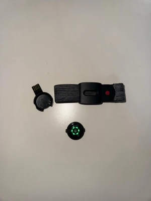 Svart pulsmätare med armband från Polar - Polar pulsmätare med svart elastiskt armband och USB-laddare. Sensorn har en grön LED på undersidan och fästs enkelt på armbandet. Perfekt för träning och aktivitetsmätning. Materialet är plast och textil, och designen är smidig och modern.