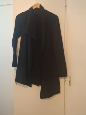Svart kappa från ONLY med draperad front - Stilren svart kappa från ONLY i storlek S. Kappan har en snygg draperad front och långa ärmar. Perfekt för dig som gillar minimalistisk och modern stil. Materialet känns mjukt och följsamt, vilket gör den bekväm att bära.