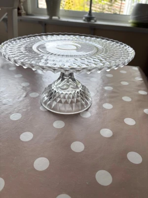 Glasfat på fot med mönster - Säljer ett elegant glasfat på fot med vackert slipat mönster. Fatet är runt med räfflad kant och har en stabil fot som också är dekorerad. Perfekt för att servera kakor, tårta eller frukt och blir en snygg detalj på bordet. Kolla gärna mina andra annonser❗️
