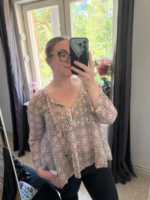 Mönstrad boho-blus med volanger - Säljer en luftig blus i boho-stil med ljusrosa botten och svart mönster. Blusen har v-ringning, volangdetaljer och långa ärmar. Perfekt till jeans eller kjol för en avslappnad look. Från märket Odd Molly i storlek 3 som enligt deras storlekguide motsvarar en storlek L. Jag har vanligtvis en 4/XL. Men denna är något liten på mig. Mycket fint skick, jag hittar inga synliga anmärkningar eller defekter. 