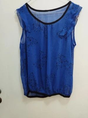 Blå transparent blus med volang och döskallar - Blå transparent blus med volang vid axlarna. Tyget har ett diskret tryck med små dödskallar och stjärnor. Svart kant vid halsringning och nederkant. Perfekt för dig som vill sticka ut med en edgy look. Se mått på bilder och se gärna mina andra annonser <3