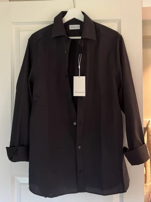 Svart skjorta från These Glory Days - Stilren svart skjorta från These Glory Days i slim fit-modell. Skjortan har klassisk krage och knappar framtill. Perfekt för dig som gillar en enkel och modern look. Fick den i present men vill ha i en annan färg så har inte äns tagit bort lappen allt är kvar. Skick 10/10. Har i både S och M. Nypris: 799kr