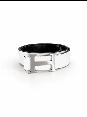 Vitt skärp med silverfärgat H-spänne - Snyggt vitt skärp i skinn med ett stort, silverfärgat H-format spänne. Bältet har en stilren och modern look med svart insida och passar perfekt till jeans eller kostymbyxor.