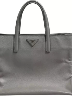 Grå handväska i läder från Prada - Snygg grå handväska från Prada i strukturerat läder med två topphandtag och klassisk triangellogo framtill. Väskan har en stilren, rektangulär form och passar perfekt till dig som gillar minimalistisk design och exklusiva detaljer. 0685 