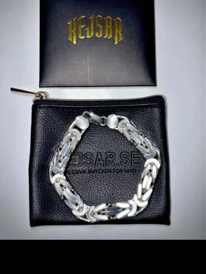 Silverfärgat kedjearmband Kejsar - Helt ny oanvänd. Snyggt och robust armband i silverfärg från Kejsar. Armbandet har en bred, platt kedjedesign med blanka länkar och stämplad 925 på låset, vilket tyder på äkta silver. Perfekt accessoar för dig som gillar stilrena och tunga smycken.10mm 22cm 111gram