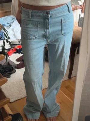 Ljusblå raka jeans med fickor fram - Säljer ett par ljusblå jeans med raka ben och höga fickor framtill. Jeansen har en avslappnad passform och klassisk knappgylf. Perfekta för en chill och trendig look. Materialet är denim i bomull.