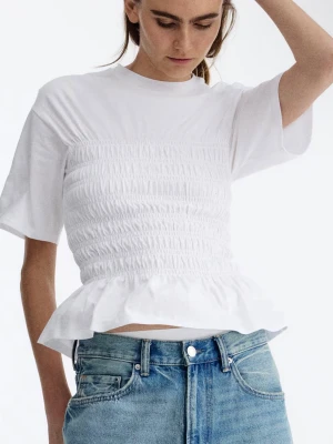Vit smockad topp med volang - Säljer en söt vit topp med smockad midja och volangkant nedtill. Toppen har korta ärmar och en croppad passform som ger en trendig look. Perfekt att matcha med höga jeans eller kjol.