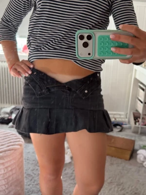 Svart volangkjol i denim - Säljer en svart kortkjol i denim med volangkant nedtill. Kjolen har klassisk jeansdesign med fickor fram och bak samt knapp och dragkedja i midjan. Perfekt för dig som gillar en edgy och trendig stil. Går att vika ner för låg midja. Den är egen sydd från ett par jeans.