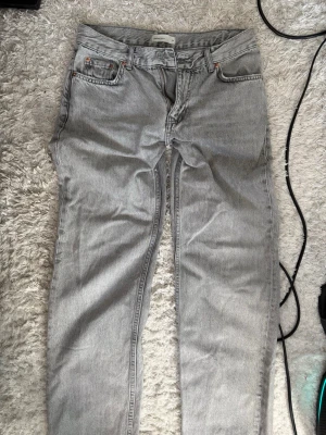 Ljusgrå raka jeans - Säljer ett par ljusgrå jeans med rak passform och klassisk femficksdesign. Jeansen har bälteshällor, knappgylf och är tillverkade i ett slitstarkt denimtyg. Perfekta för en avslappnad och trendig look.